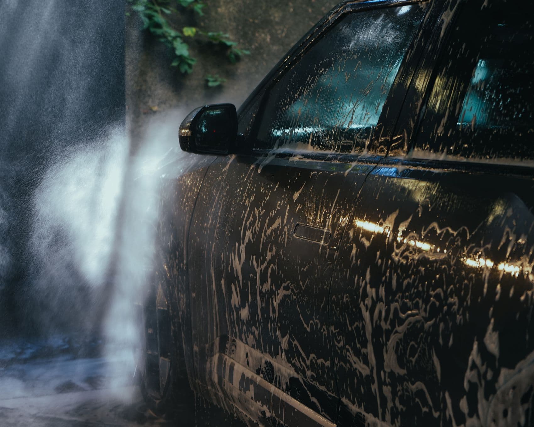 Backlit rinse water sheeting off a dark EV during a decontamination wash